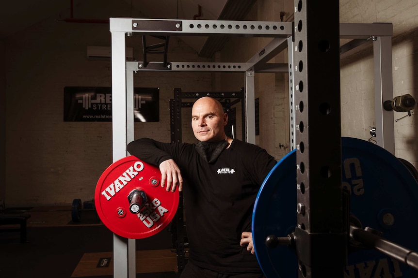 A man in black clothes stands next to a weight machine