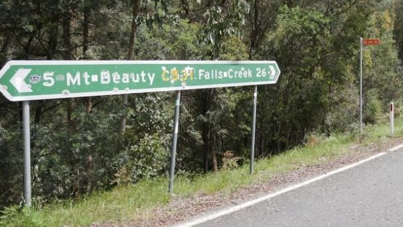 A road sign showing directions to Mt Beauty and Falls Creek, with bushland behind.