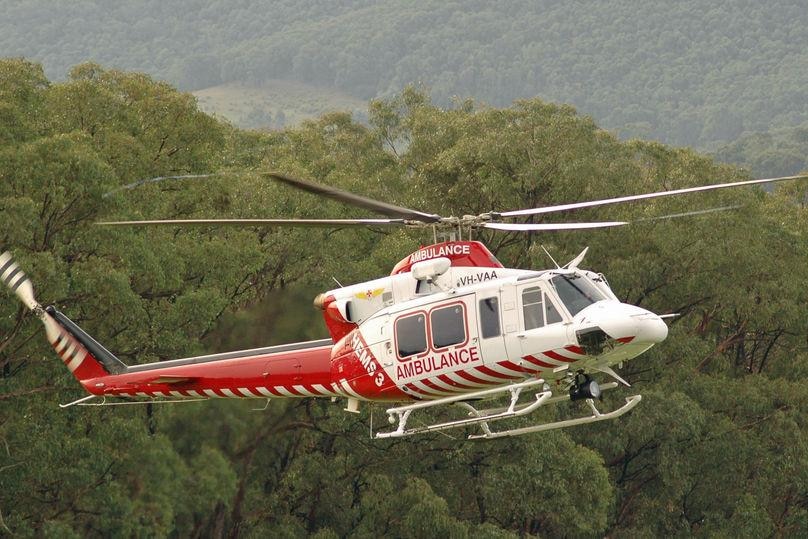 A white helicopter with red strips lands in front of trees