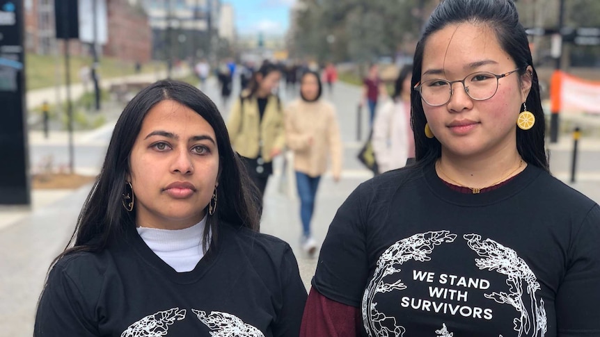 Two young women wearing t-shirts that say "We stand with survivors".