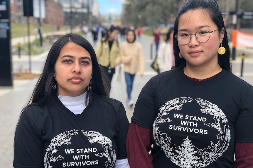 Two young women wearing t-shirts that say "We stand with survivors".