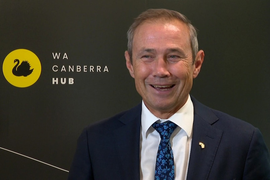 A beaming WA Premier Roger Cook next to a wall logo reading "WA Canberaa Hub".