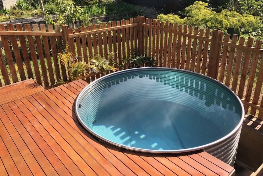 A wooden deck surrounds a steel tank filled with clear, blue water. 