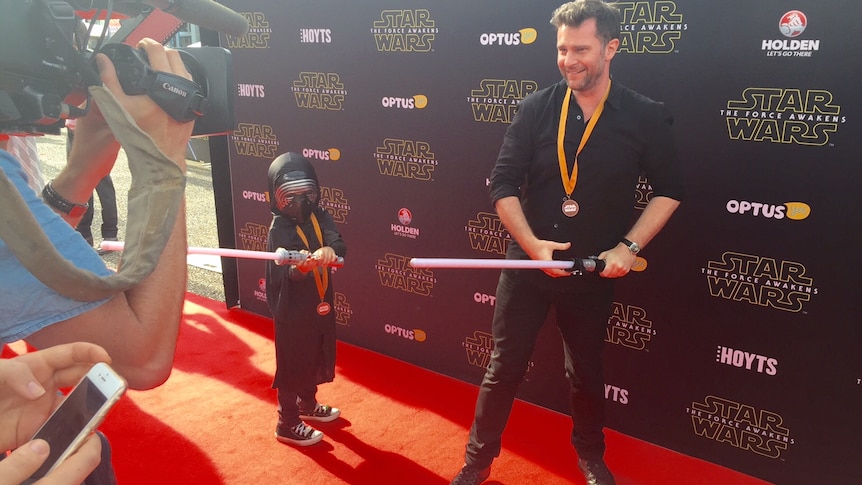 A young Star Wars fan and an older one, both wielding toy lightsabers.