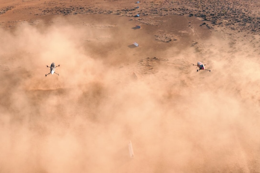 Two flying objects above a cloud of dust in a desert landscape, photographed from above.