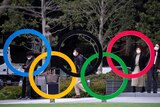 People walk past a structure of the Olympic rings in Tokyo, wearing face masks.