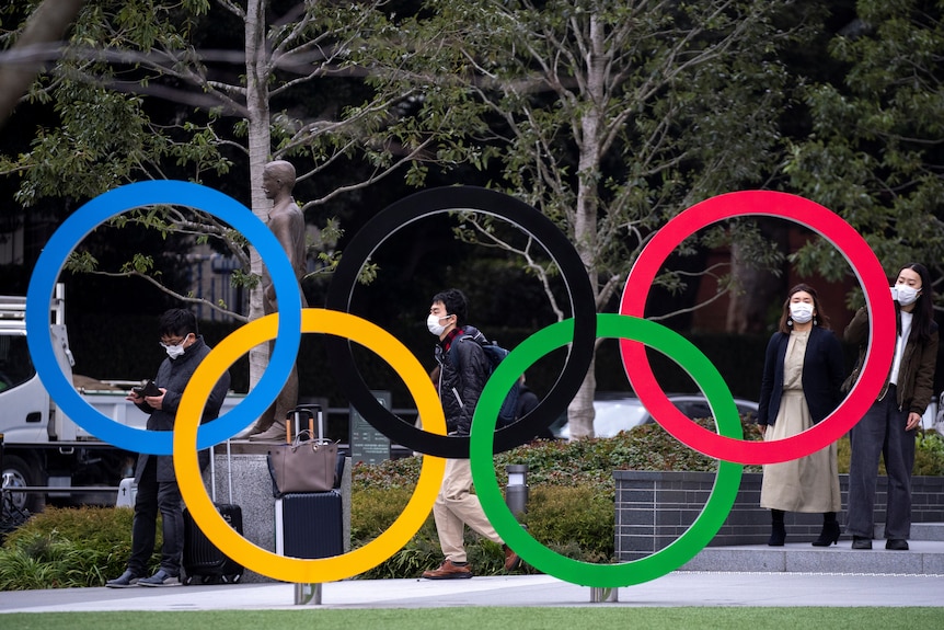 People walk past a structure of the Olympic rings in Tokyo, wearing face masks.