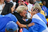 A woman wears a beaming smile as she looks at a female athlete who is wrapped in a Scottish flag after a race.