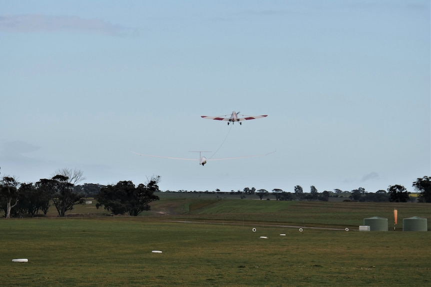 Two small planes fly off a runway connected by a rope.