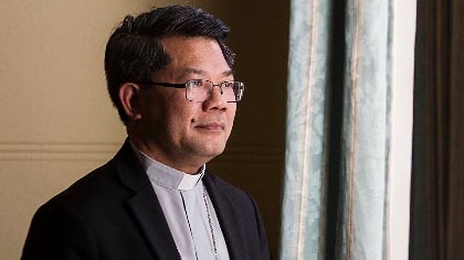 Bishop Vincent Long Van Nguyen stands next to a window and is lit by its soft light.