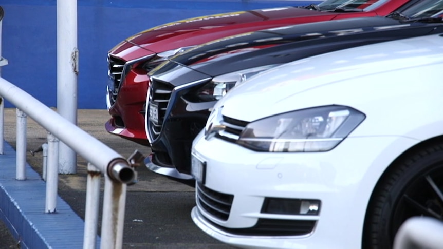 The fronts of thee cars, red, black and white, parked in a row.