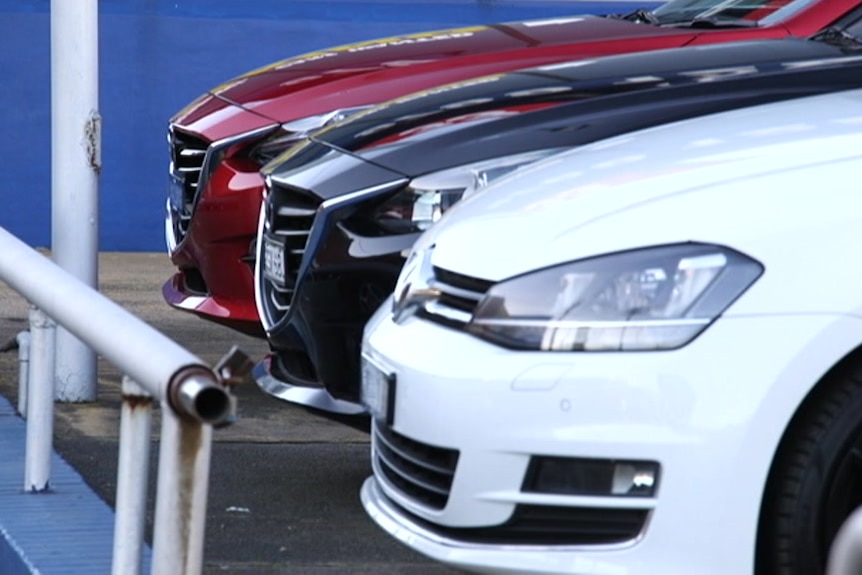 The fronts of thee cars, red, black and white, parked in a row.