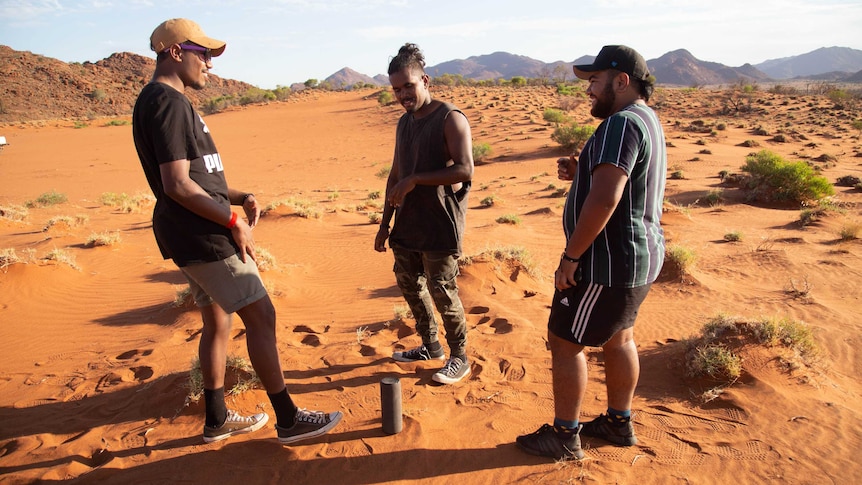 Three young boys rap on a sand hill.