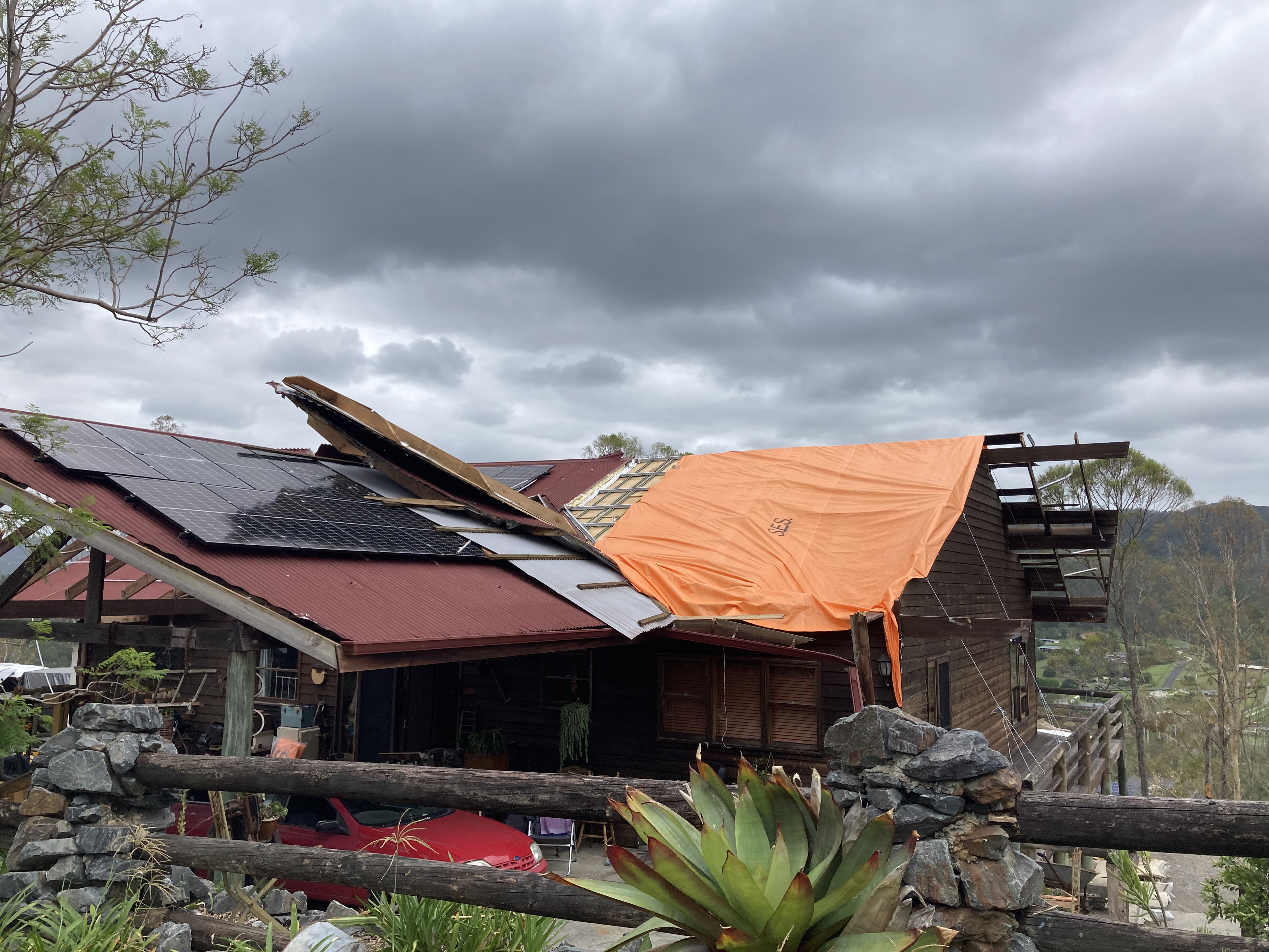 An orange tarp is draped over a roof frame after the top was blown off. 