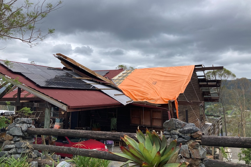An orange tarp is draped over a roof frame after the top was blown off. 