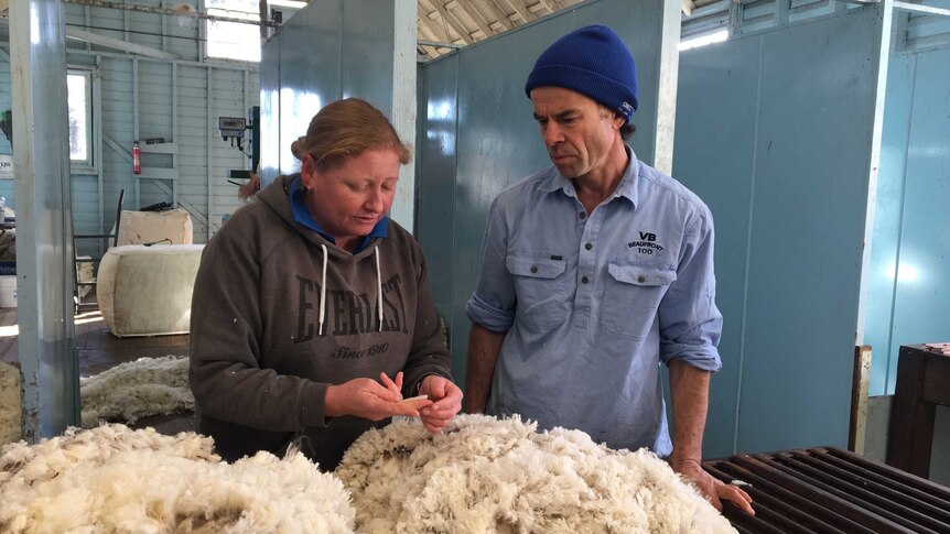 A female wool classer and a male farmer look down at a table of wool while having a conversation.