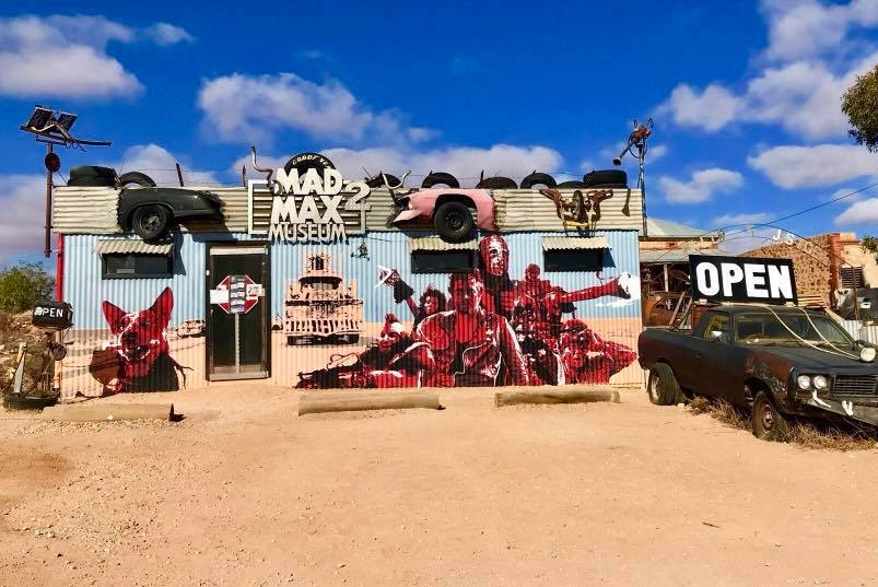 Exterior of a corrugated metal building painted with a Mad Max 2 mural.