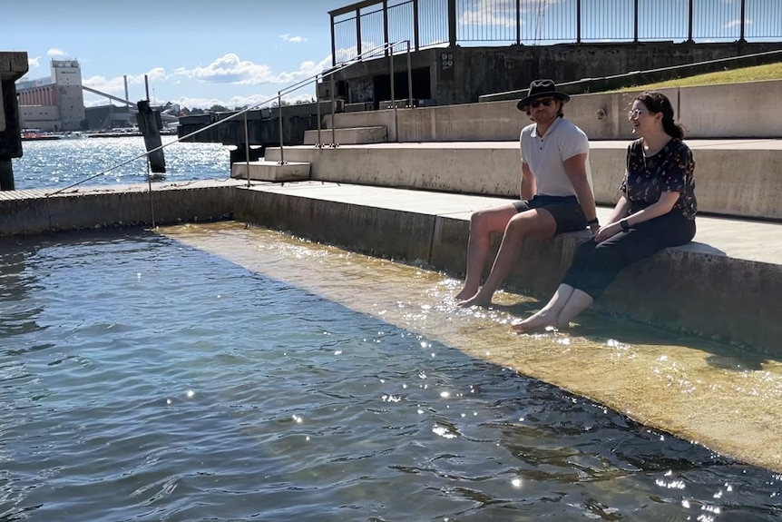 A man and a woman dip their feet in the water.