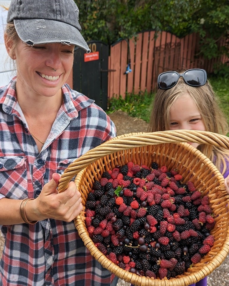 A woman and a young girl holding up a basket of mixed berries.