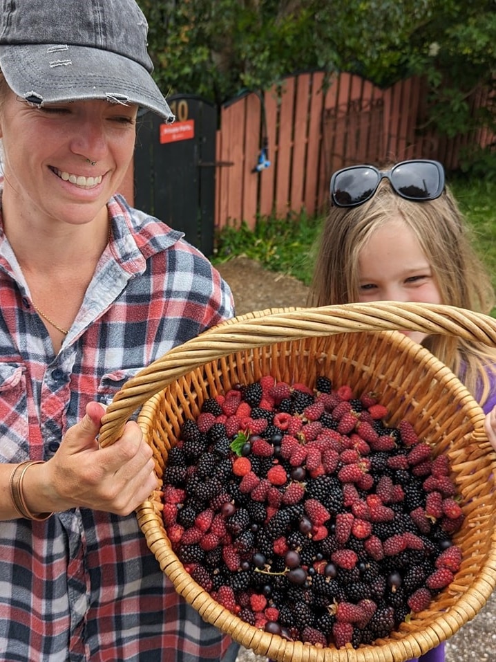A woman and a young girl holding up a basket of mixed berries.