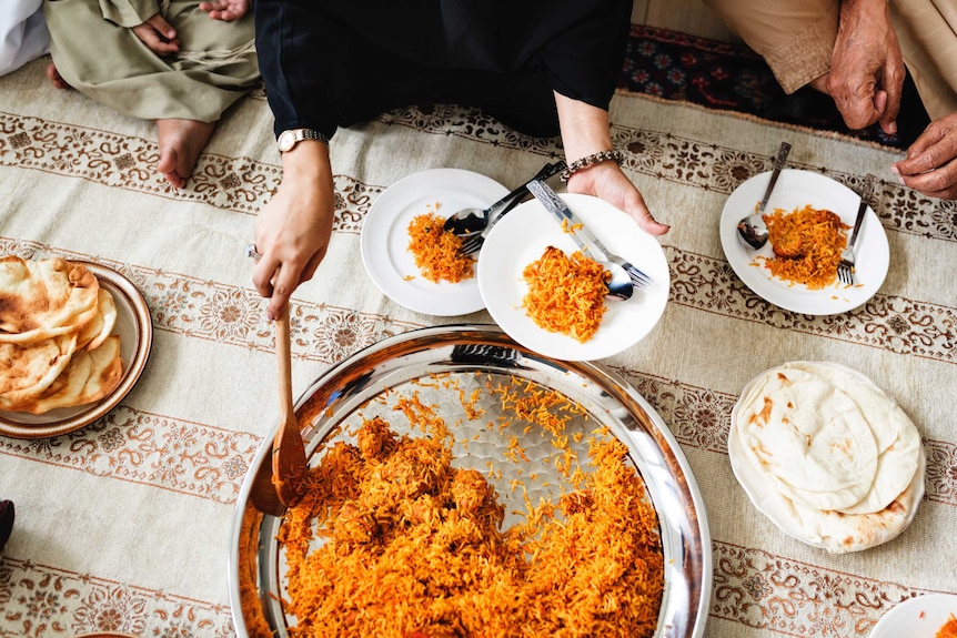 A woman serves biryani, a rice dish, from a silver dish with a wooden spoon.
