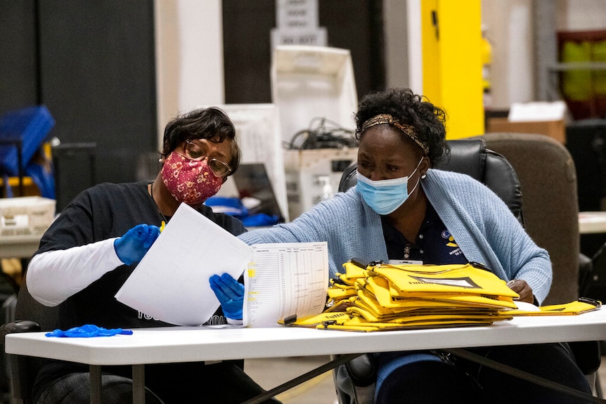 Two elections workers wearing facemasks point to a piece of paper while counting votes in Georgia.