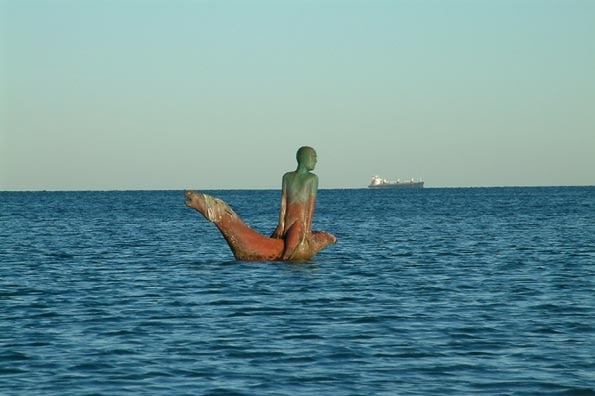 A bronze sculpture of a man on a horse in the ocean. 