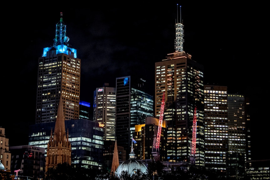 High rise buildings in Melbourne's CBD at night with lights coming through windows. 