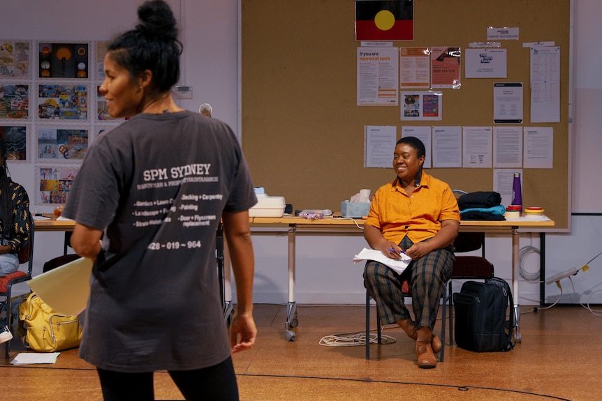 In a rehearsal room, Maxine Beneba Clarke sits smiling, a script on her lap, Zahra Newman standing in front.