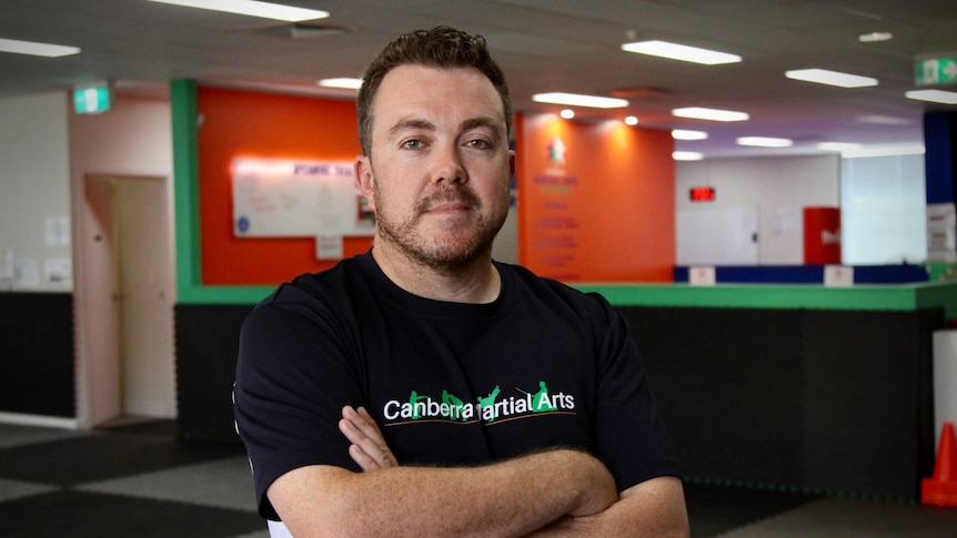 Tom stands with his arms crossed wearing a shirt that says 'Canberra martial arts'.