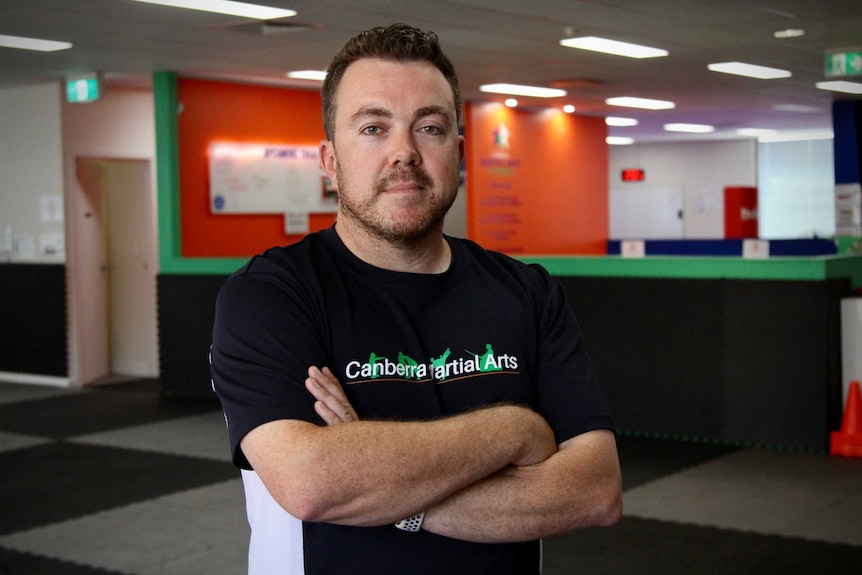 Tom stands with his arms crossed wearing a shirt that says 'Canberra martial arts'.