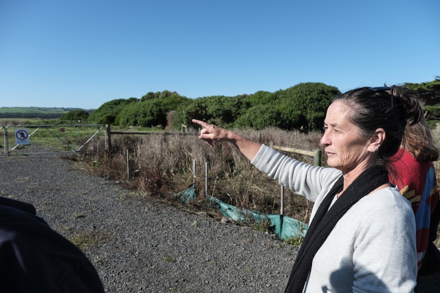 Kim stands at the site where the development will be built on a sunny blue sky day pointing out at the land.