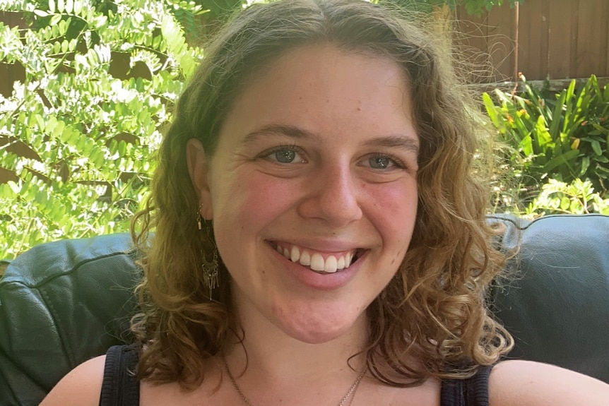 A young white woman is sitting in a garden smiling.