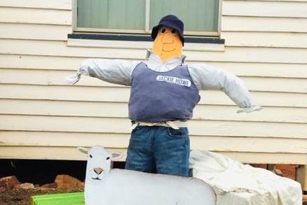 A scarecrow in a blue singlet stands in from of some scarecrow sheep