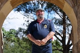 Peter Lipscomb dressed in navy blue polo top and pants in front of an arch.