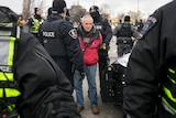 A man in a red jacket is surrounded by police and arrested.