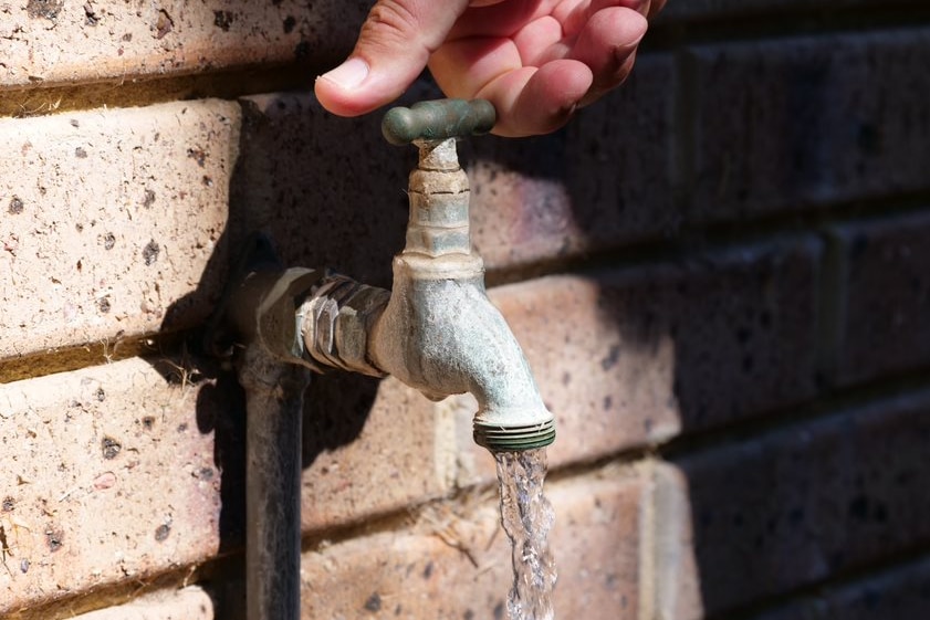 A hand turning an old, stained water tap attached to a brick wall