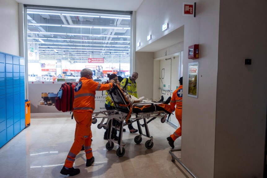 Emergency personnel wheel an injured person through a corridor on a stretcher.