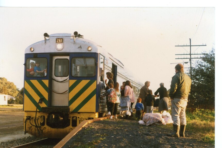 A group of people huddle on a platform at the entry of a blue and yellow train.