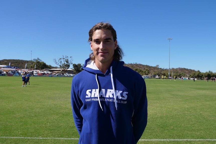A young man, wearing a blue sharks jumper and standing on a footy field