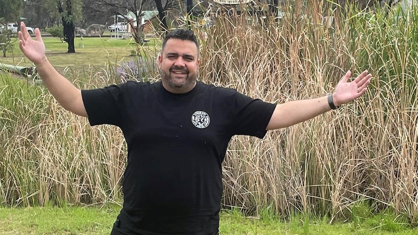 Comedian Dane Simpson standing in front of Walgett town sign.