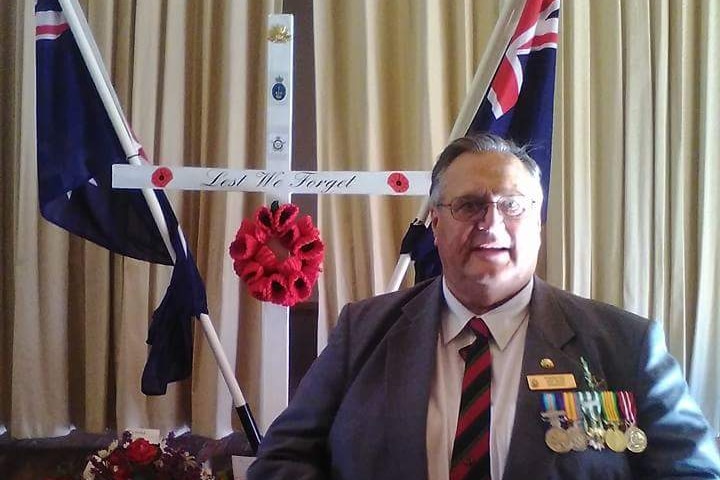 A man in a grey suit wearing service medals in front of a military style funeral