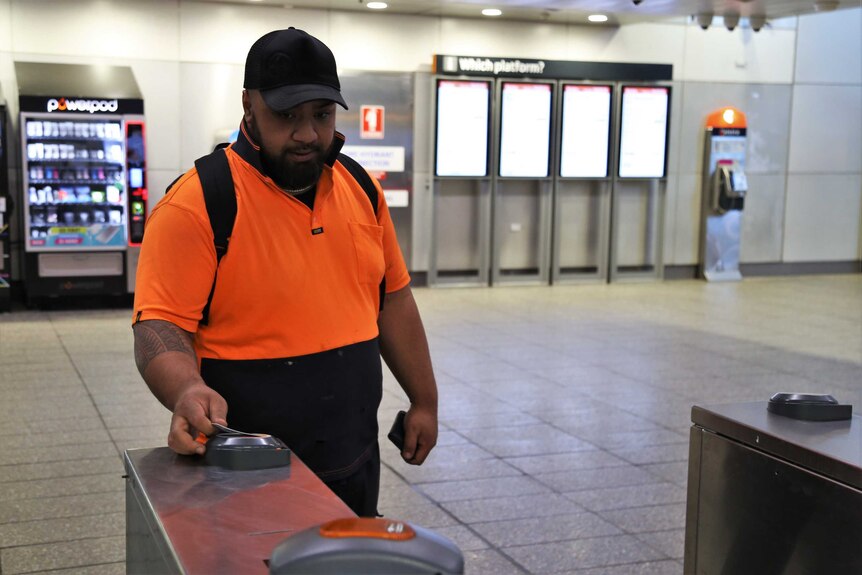 Man in orange shirt puts his Opal card against the reader at a Sydney train station.