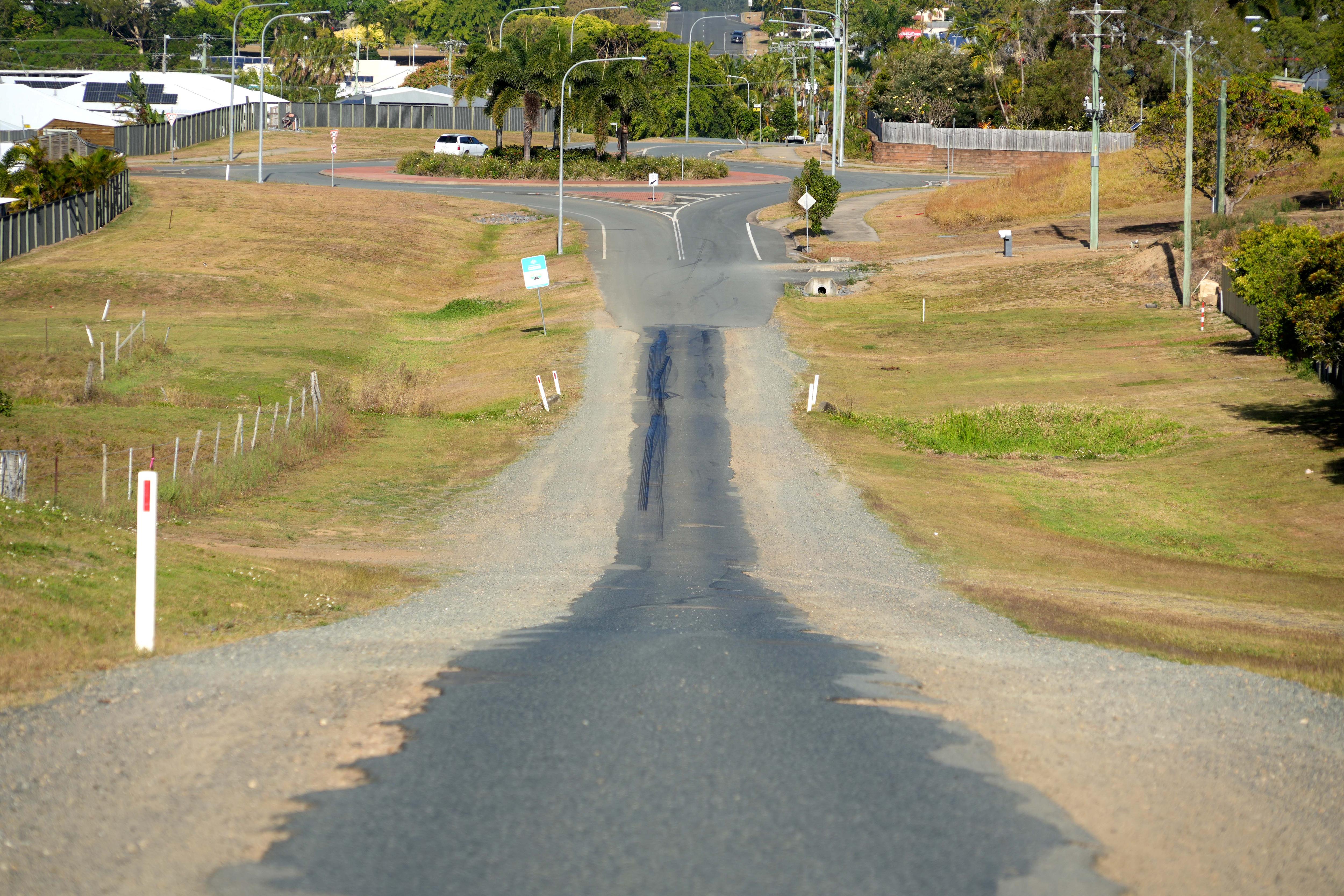 A sealed bitument road showing a downhill dip with grass on either side.