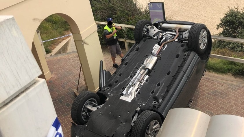 a car flipped over on a pedestrian path next to a beach