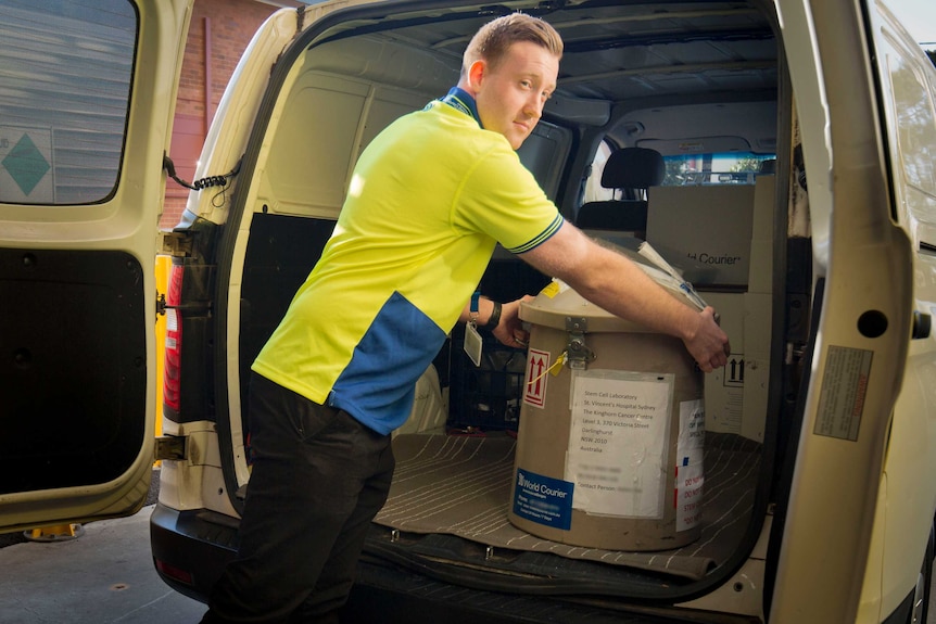 A man takes a cylindrical tank containing frozen stem cells from the back of a delivery van.