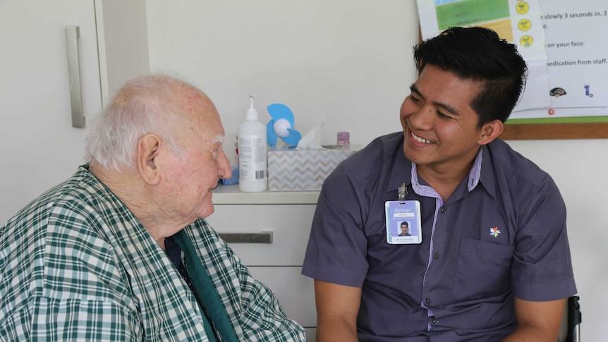 An elderly patient smiles as he talks to a young male nurse