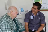 An elderly patient smiles as he talks to a young male nurse