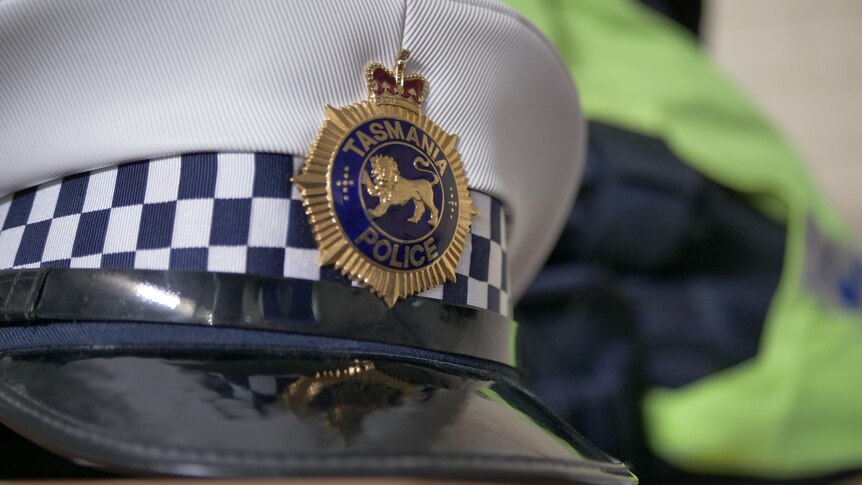 A gold and blue badge of a white cap reads Tasmania Police