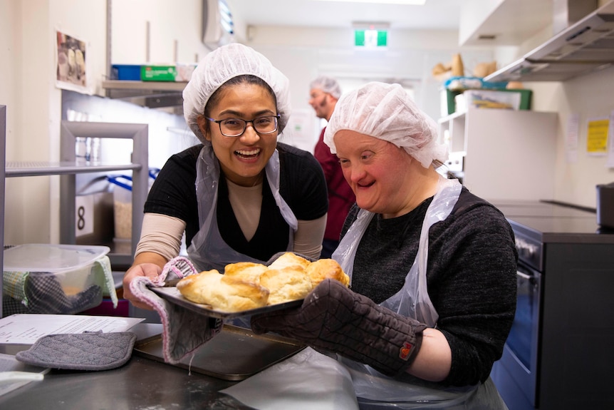 Two women hold a tray of scones they have baked.